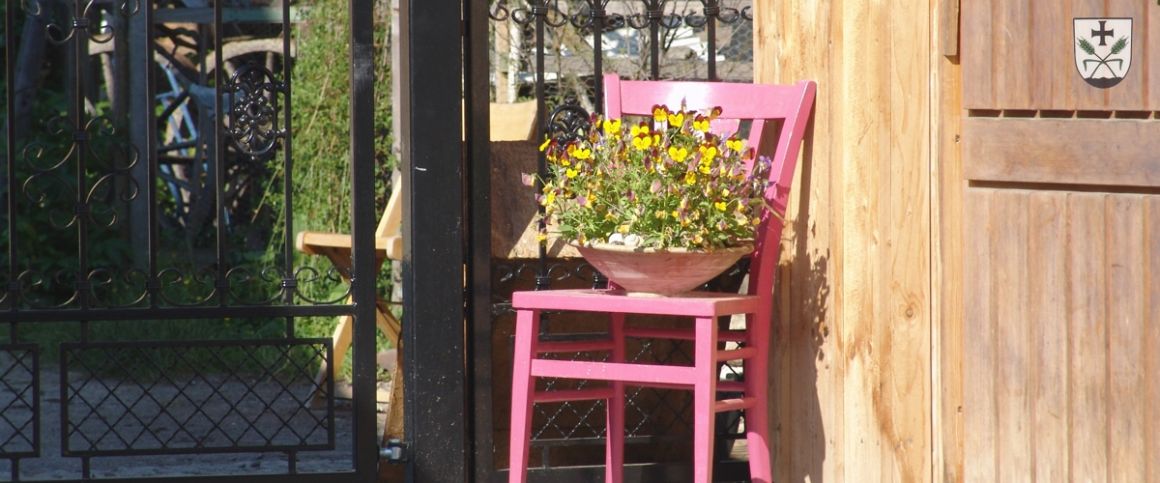 Dorfimpression / rosa Stuhl vor Gartentor